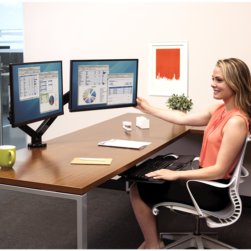 žena sedící u stolu s držákem pro dva monitory vedle sebe