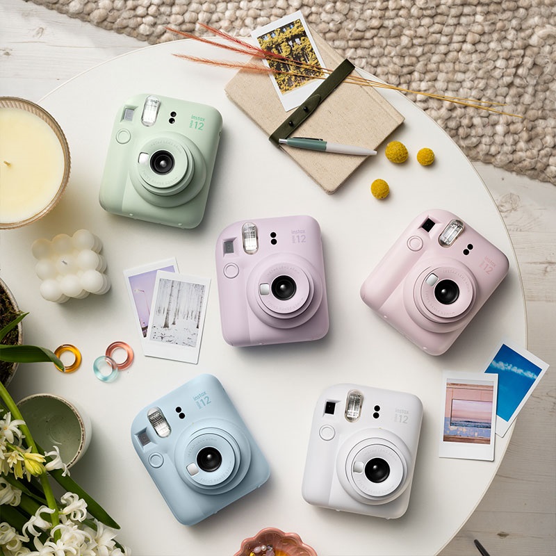 Fotoaparáty Fujifilm Instax mini 12 v rôznych farbách umiestnené na stolíku