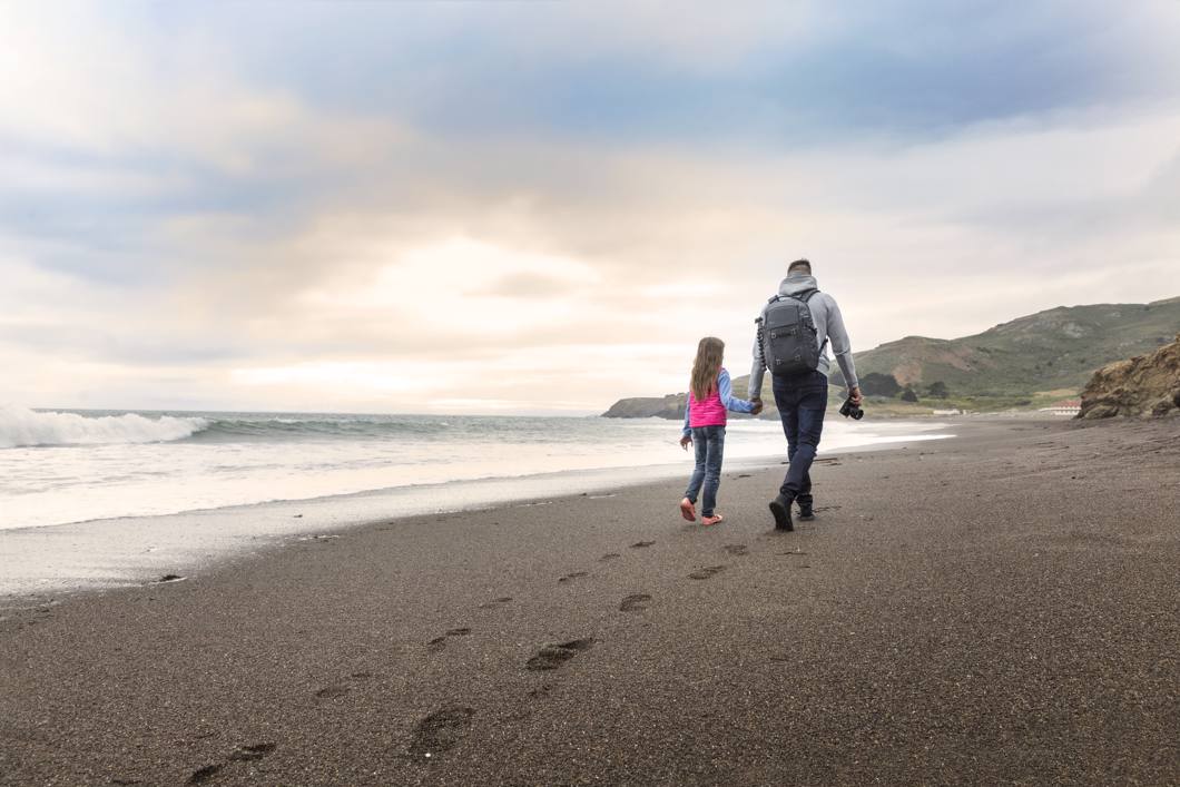 Fotograf na pláži se svou dcerou a batohem Lowepro Freeline.