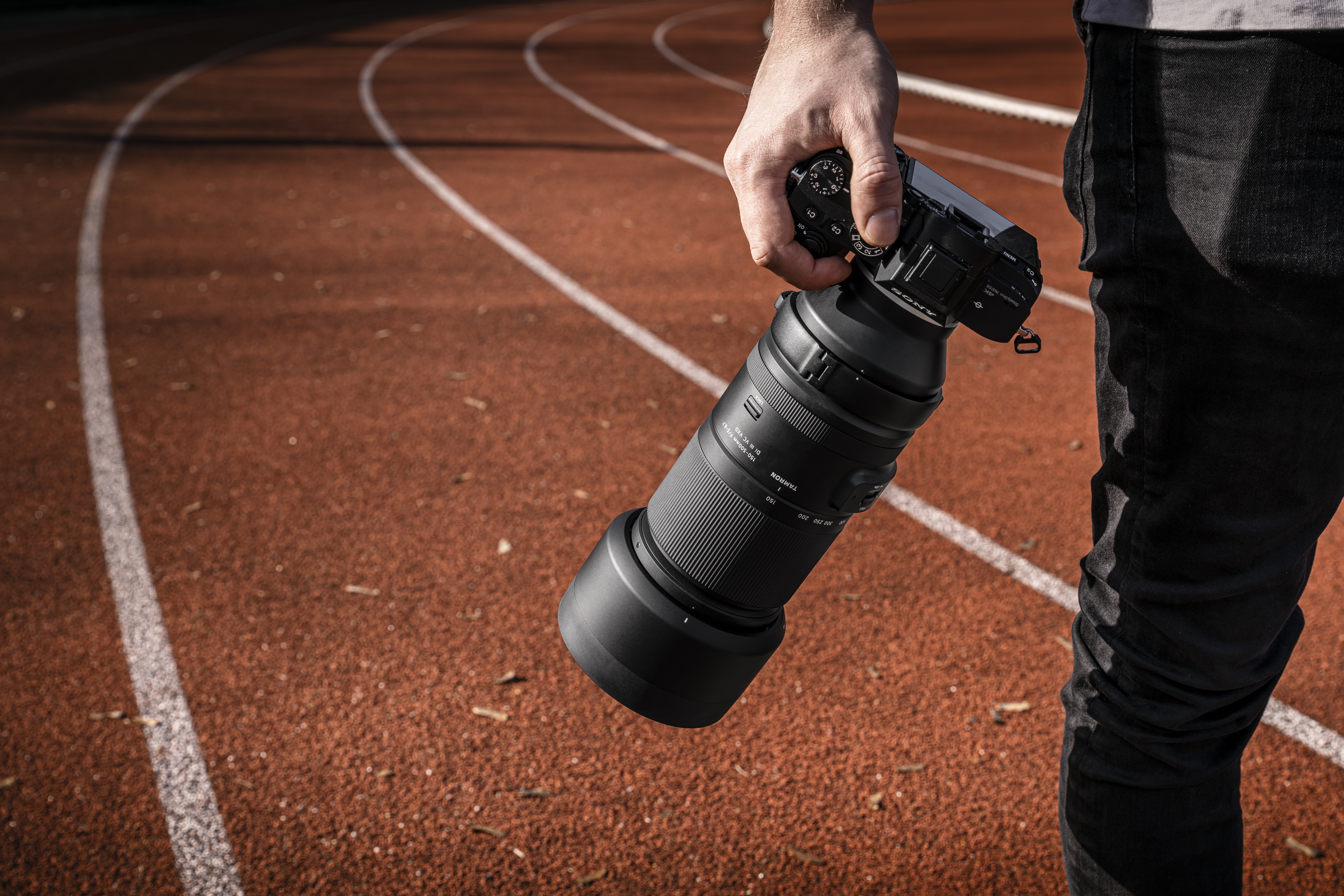 Objektiv Tamron na fotoaparátu Sony v ruce fotografa na běžecké dráze