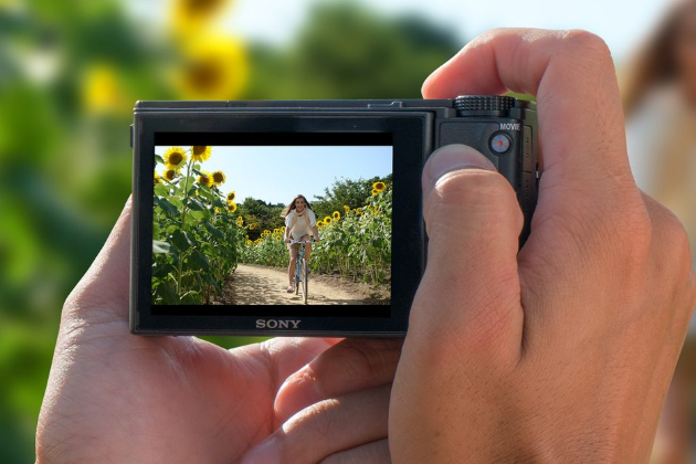Digitálný fotoaparát Sony DSC-RX100V,na obrázku je dievča na bicykli medzi slnečnicami